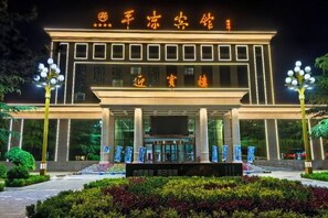 A hotel entrance with illuminated signage, a central entrance with steps, and a landscaped garden area. - Pingliang Hotel (Pingliang)