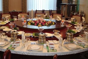 A round dining table with a floral centerpiece, surrounded by chairs and set with fine china, glassware, and silverware.