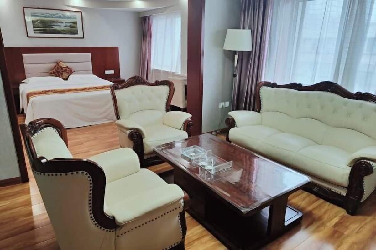 A hotel room with a bed, two armchairs, a sofa, a wooden coffee table, and a lamp.
