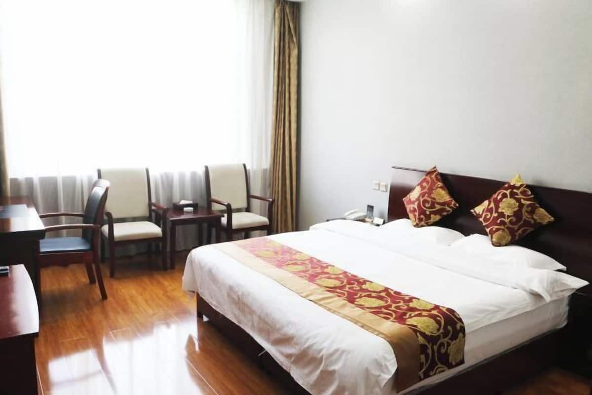 A hotel room with a bed, a desk, two chairs, a telephone, and a window with curtains.
