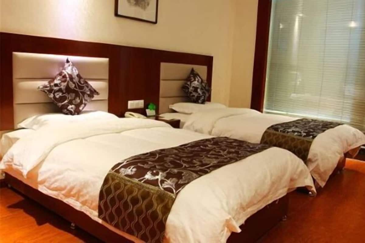 A hotel room with two beds, each with a headboard, a bedside table, and a lamp.