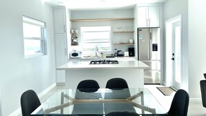 A modern kitchen with a central island, white cabinetry, and a dining area with a glass table and chairs. - The Luxury Escape - Peaceful & Charming 3-bedroom villa w/ sea view (Vieux Fort)
