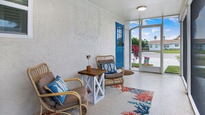 Un solárium con sillas de mimbre, una mesita y una puerta azul que da al exterior.