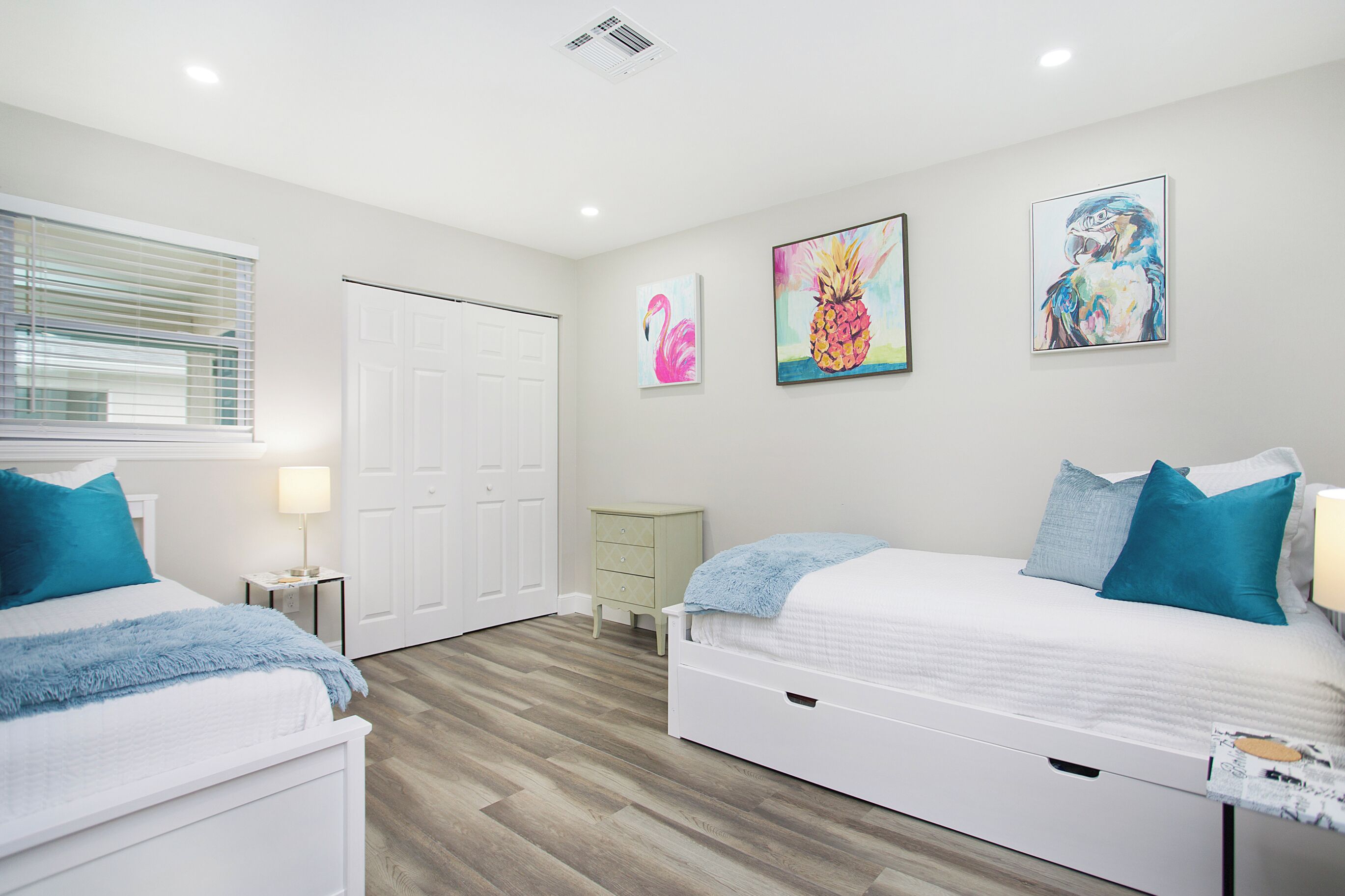 A bedroom with two beds, a nightstand, a dresser, and artwork on the walls.