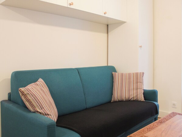 A teal sofa with striped pillows, a dark throw, and a wooden coffee table with a patterned edge.