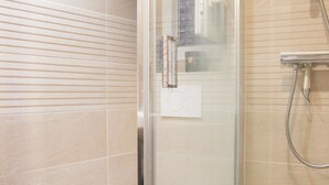 Eine Dusche mit Glastür, einer Handbrause und einem fest installierten Bedienfeld.