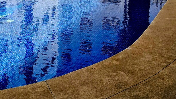 Una piscina con borde de azulejos, rodeada por un edificio con varias ventanas y balcones.