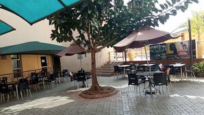 An outdoor seating area with tables and chairs, a central tree, and umbrellas providing shade. - Continental Suites Ltd (Abeokuta)