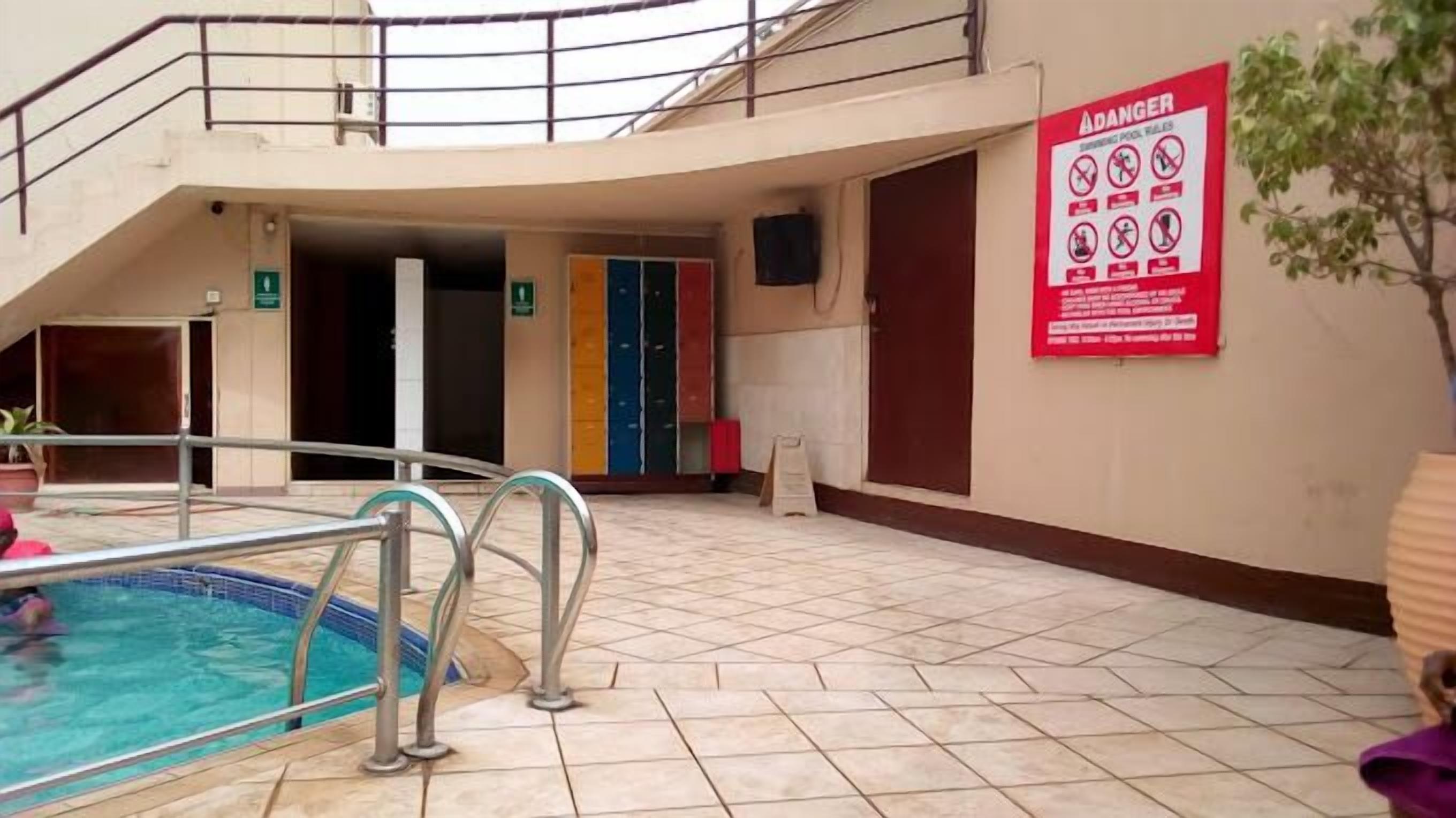 An indoor swimming pool with a safety sign, tiled flooring, and a staircase leading to an upper level.
