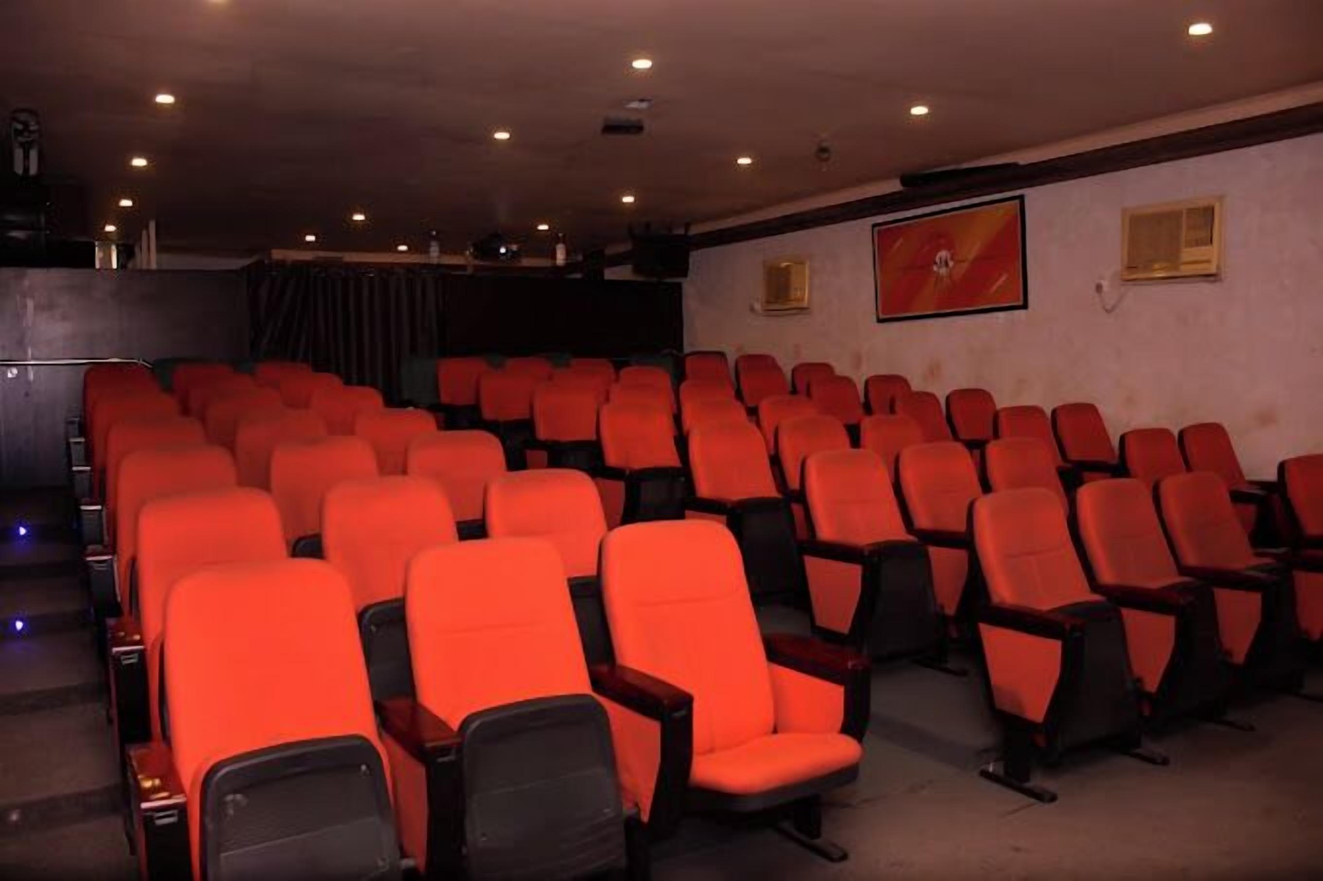 A theater with rows of red seats, a stage, and a red wall with a clock.