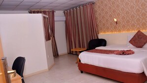 A hotel room with a bed, a chair, a small table, and curtains. - Continental Suites Ltd (Abeokuta)
