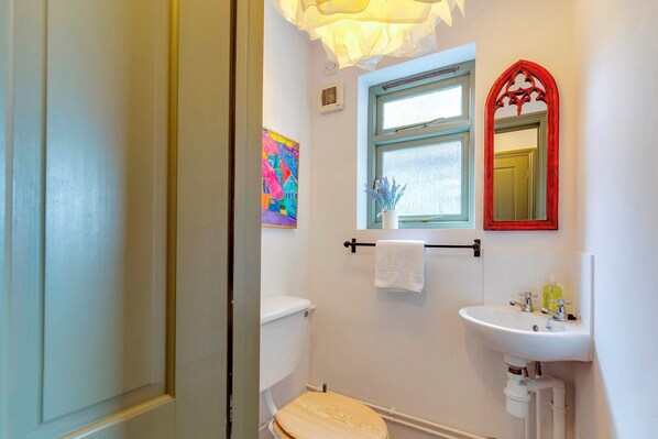 A bathroom with a toilet, sink, and window. There is a towel rack above the sink and a painting on the wall.