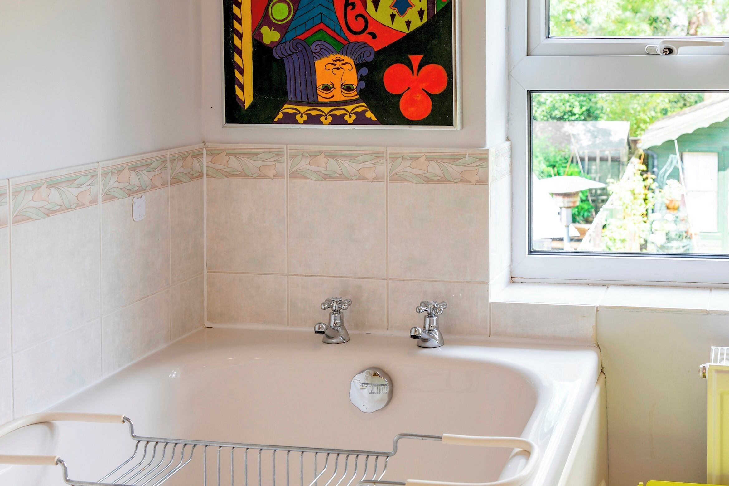 Une salle de bain avec une baignoire, deux robinets, une pomme de douche et une fenêtre donnant sur le jardin.