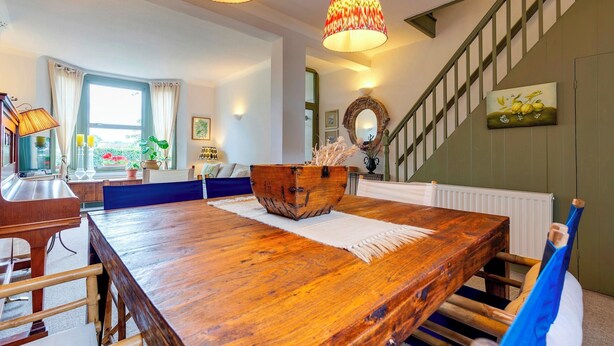 A dining area with a wooden table, chairs, and a decorative bowl centerpiece. A staircase with a railing and a painting is visible in the background. - Pass the Keys | Charming Victorian Terrace in centre of Cambridge (Cambridge)