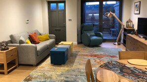 A modern living room with a grey sofa, a blue ottoman, a wooden side table, a wooden dining table with chairs, a blue armchair, and a large window with a view of the outside. - Boutique private apartment convenient for city - Pass the Keys (Bath)