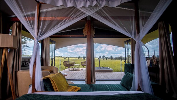 Una cama con dosel, vistas al exterior, una silla y una mesa en una terraza.