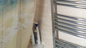 Un baño con cortina de ducha con una escena de playa, un perchero y una botella de jabón de manos en el suelo.