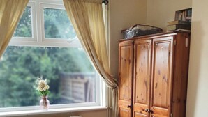Un dormitorio con cama, ventana con cortinas, radiador y armario de madera.