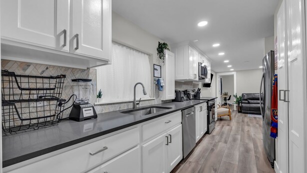 A modern kitchen with white cabinets, a black countertop, and stainless steel appliances. - Home Base for Winter Ski Adventure & Salt Lake City Events (Sandy)