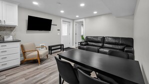 A modern living room with a black leather sofa, a wooden dining table, and a TV mounted on the wall. - Home Base for Winter Ski Adventure & Salt Lake City Events (Sandy)
