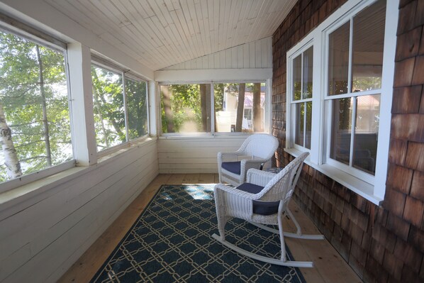 A covered porch with a rocking chair, large windows, and a patterned floor mat.
