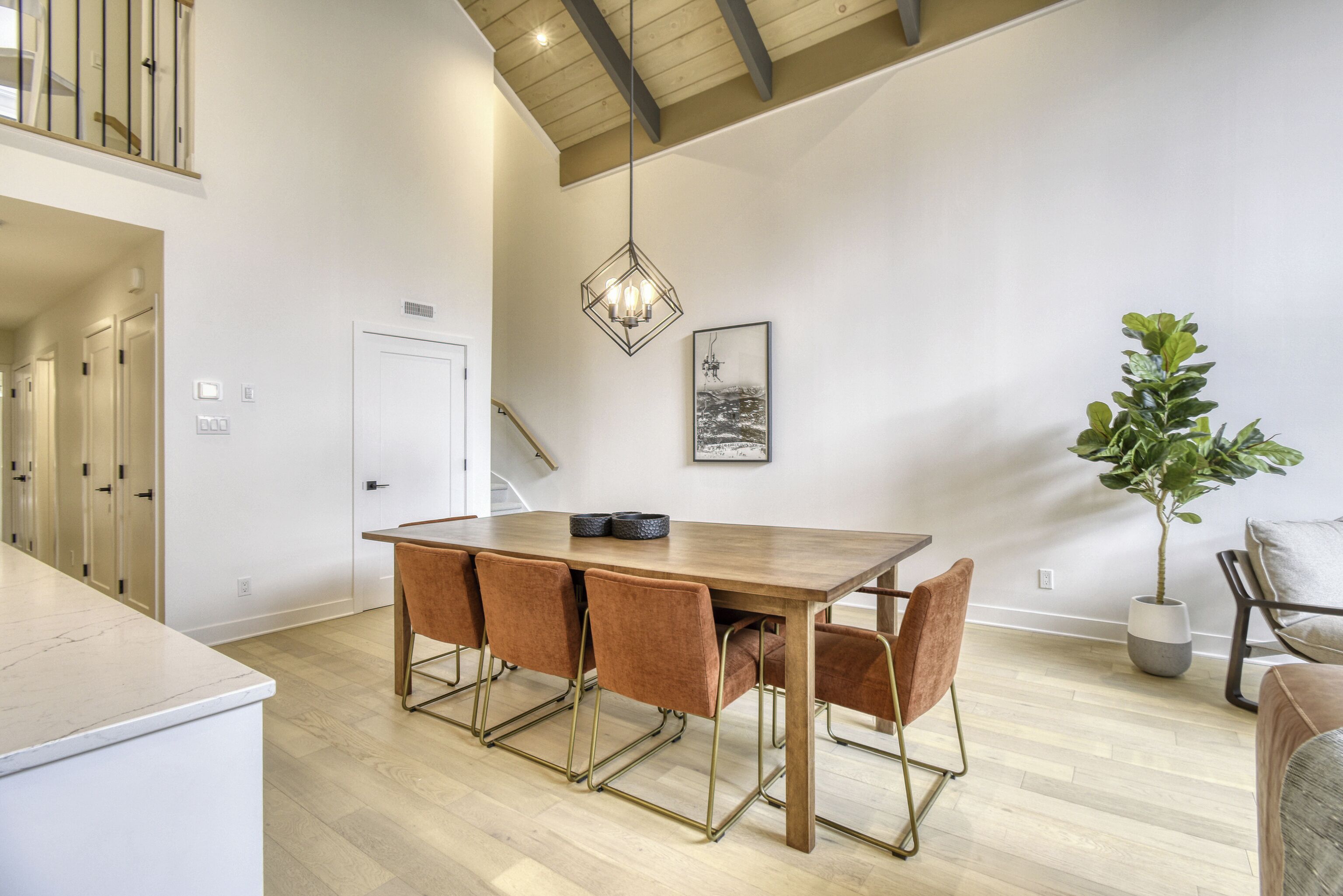 A spacious dining area with a wooden table and four chairs, a potted plant, and a chandelier.