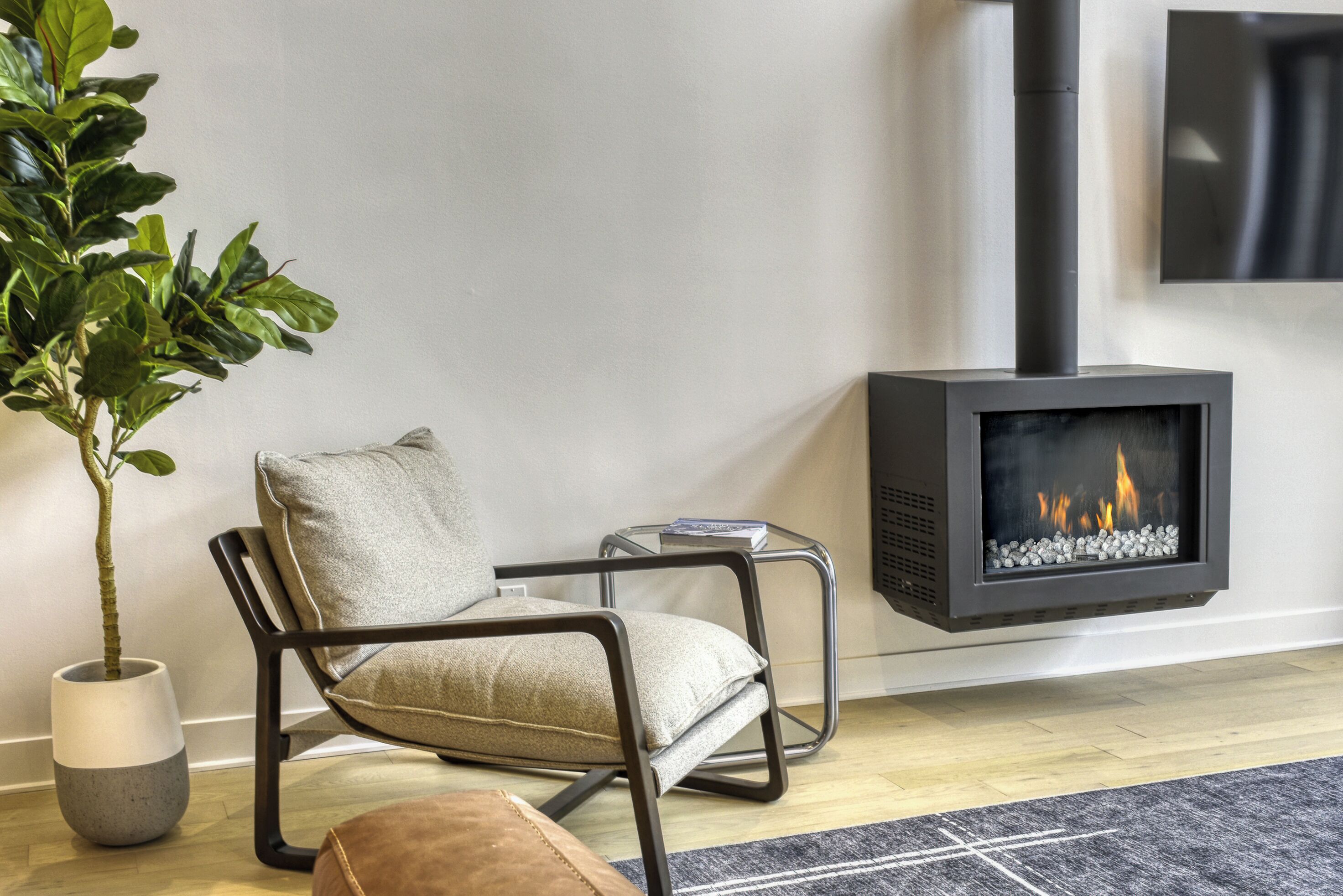 A modern living room with a black fireplace, a grey sofa, a potted plant, and a small side table.