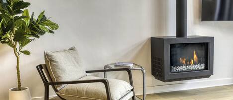 A modern living room with a black fireplace, a grey sofa, a potted plant, and a small side table.