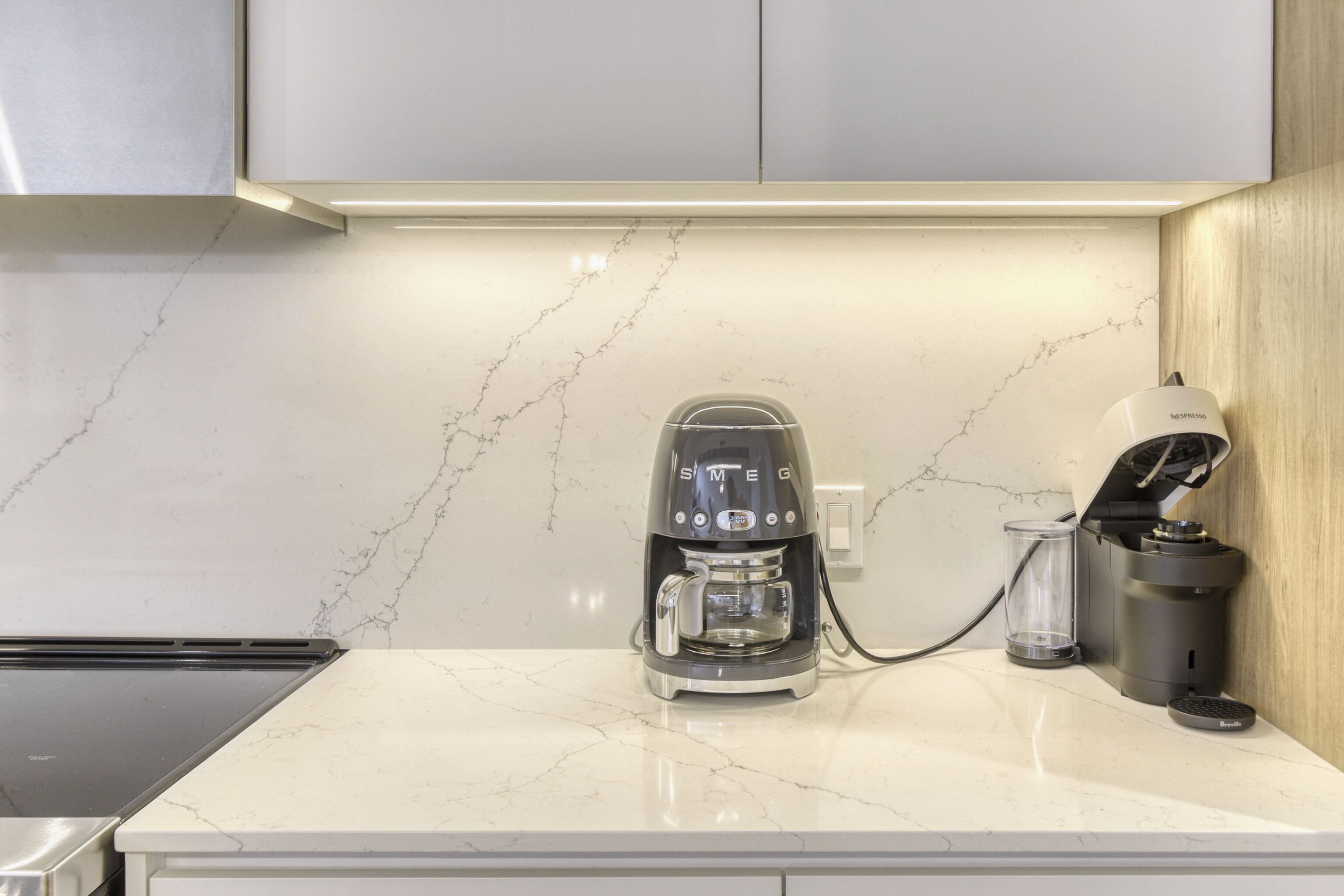 Una cocina con cafetera, un recipiente de vidrio y un hervidor sobre una encimera de mármol.