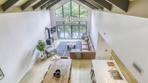 Ein geräumiges Loft mit hohen Decken, einem großzügigen Essbereich, einer gemütlichen Sitzecke mit einer Couch und Blick ins Freie durch große Fenster.