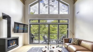 Ein modernes Wohnzimmer mit Kamin, großem Fenster und Balkon mit Gartenmöbeln.