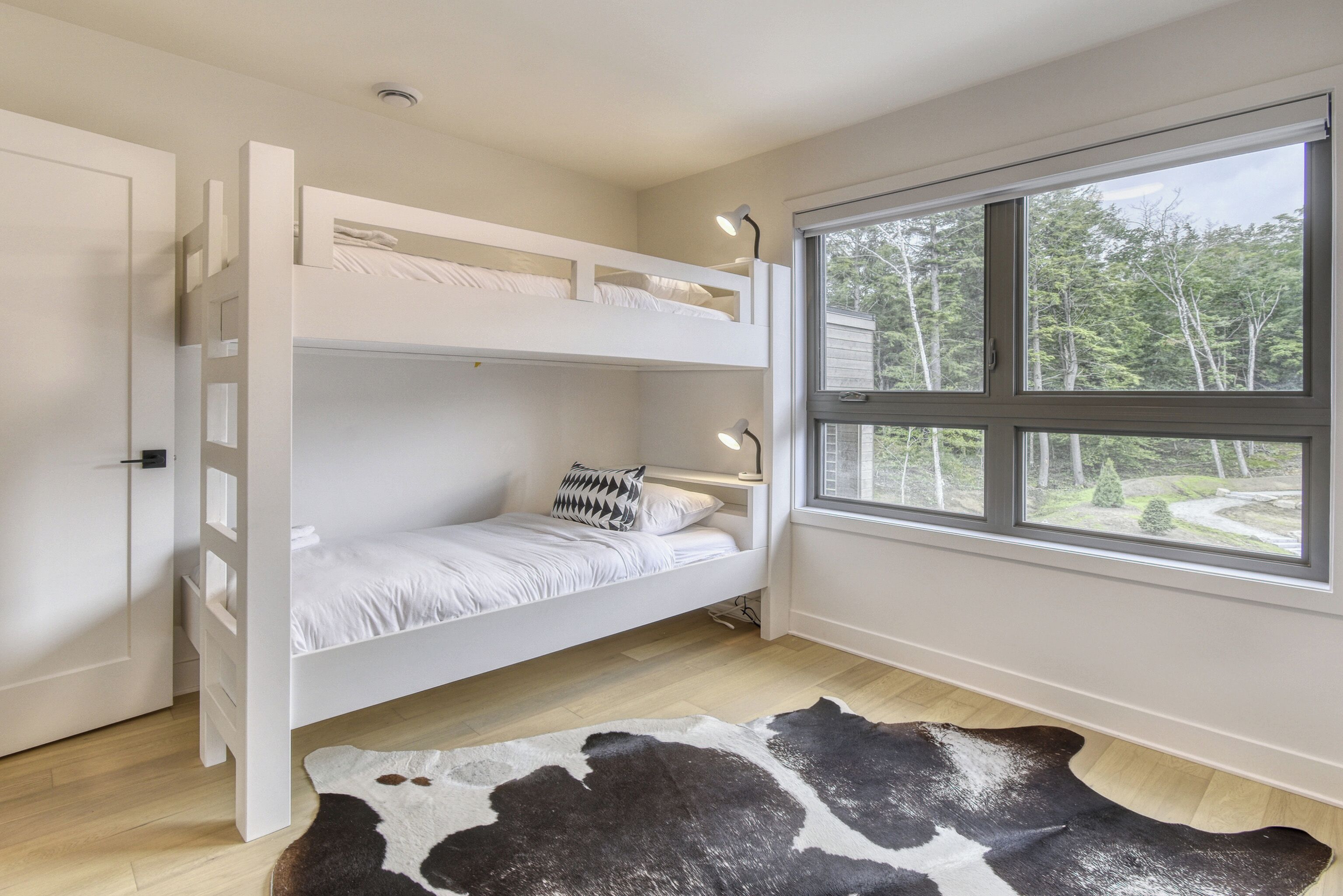A bunk bed with two levels, a window with a view of trees, and a cowhide rug on the floor.