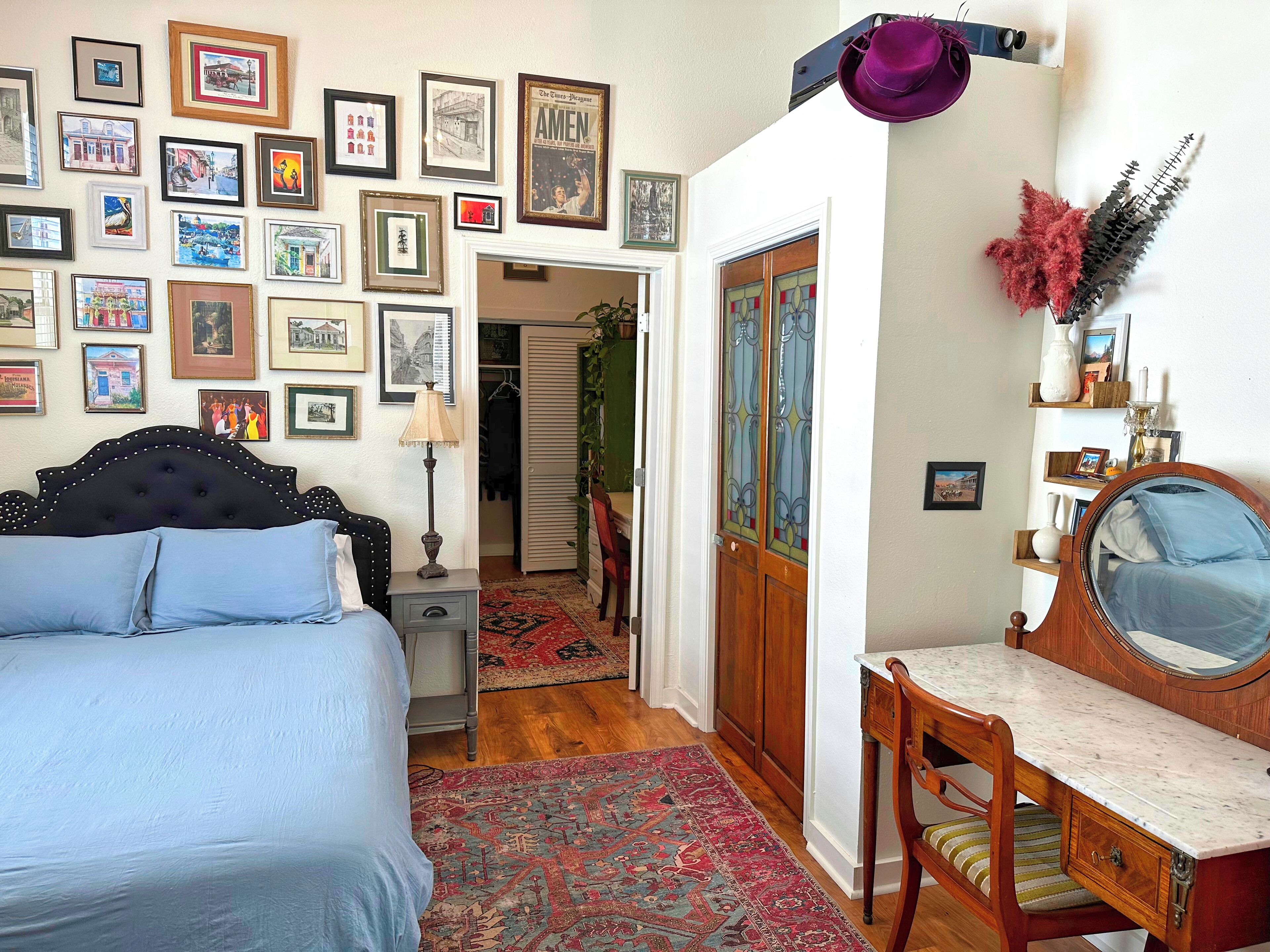Un dormitorio con una cama, un escritorio y una silla. Hay cuadros en la pared y una puerta con ventana.