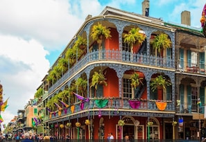A historic building with balconies adorned with plants, a red facade, and a wrought iron balcony railing.