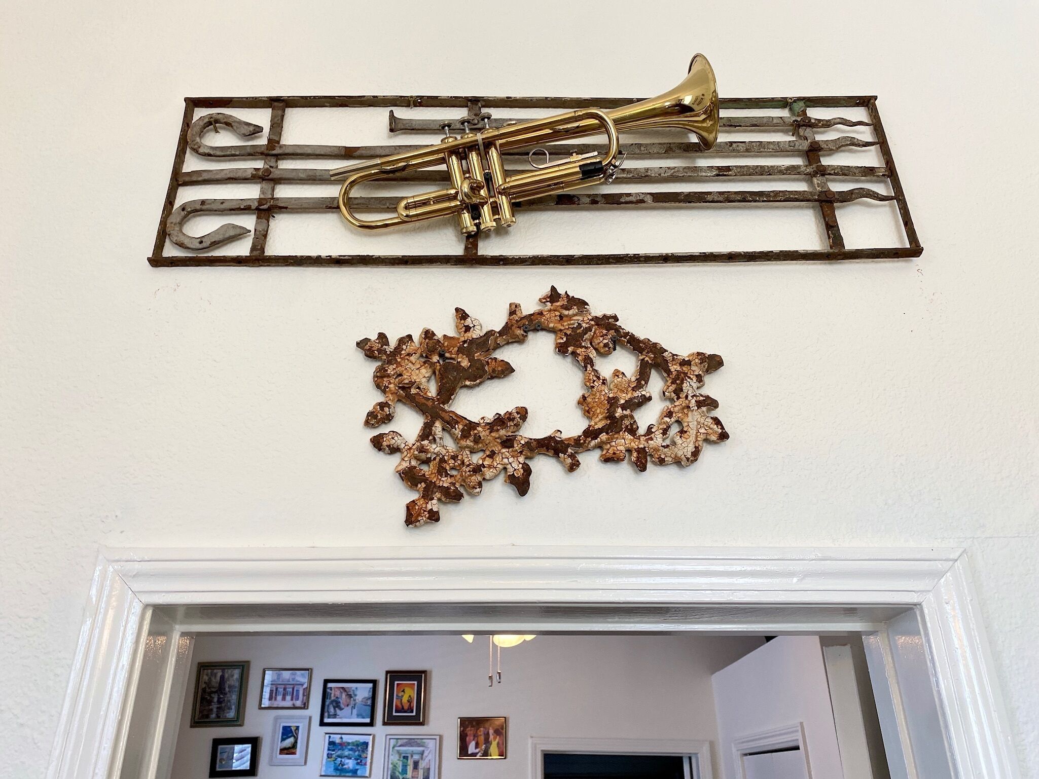 Una trompeta de latón montada sobre una celosía metálica, encima de un detalle decorativo en la pared.