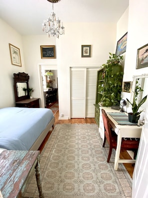 A bedroom with a bed, a desk, a chair, a chandelier, and a potted plant.