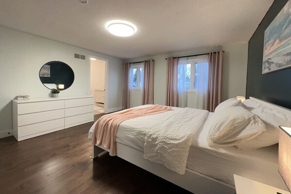 A bedroom with a bed, a dresser, a mirror, and a window with curtains.