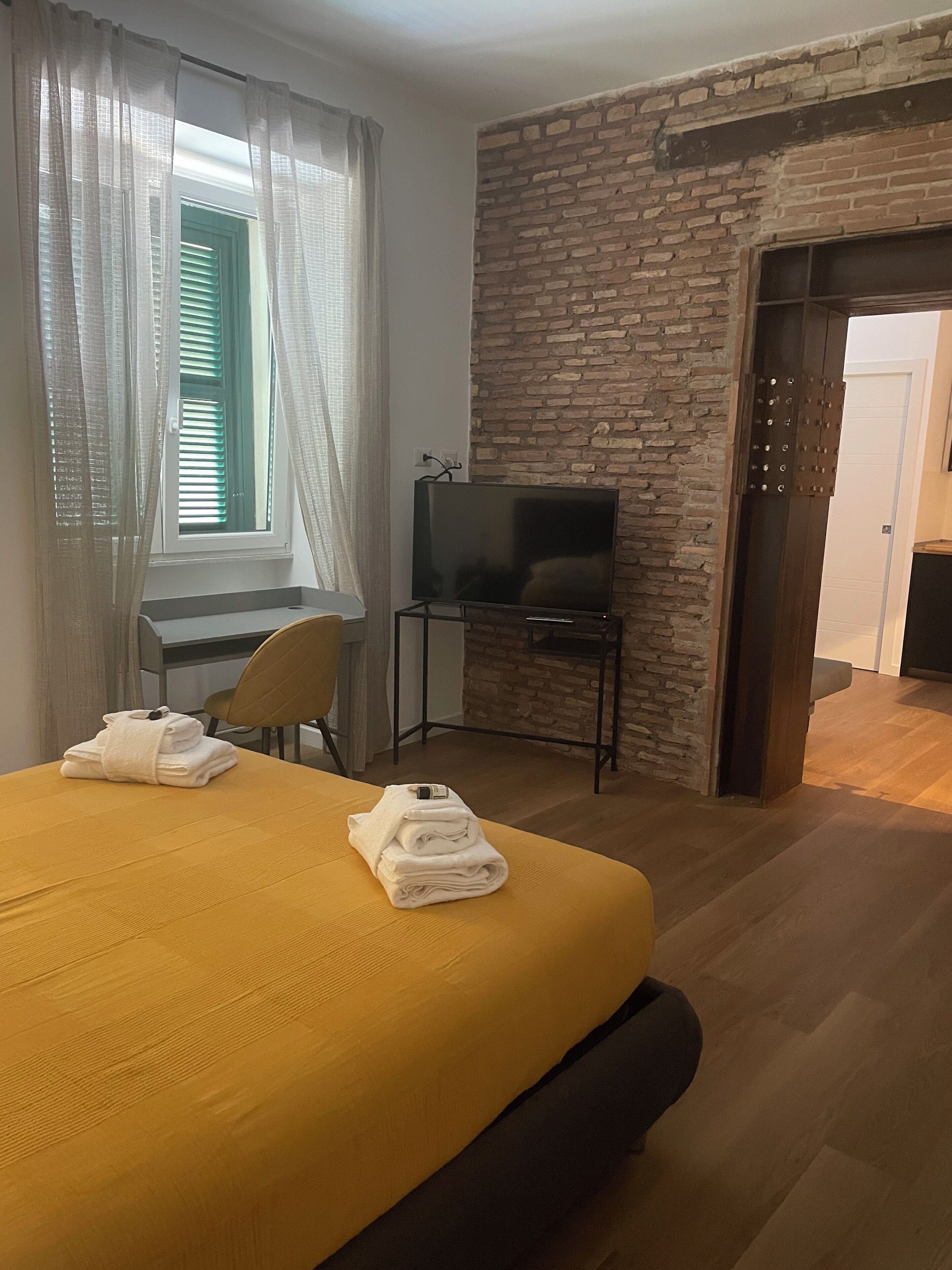 Habitació d'hotel amb llit, escriptori amb cadira, televisió i paret de maó.