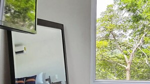 A room with a large mirror reflecting a bed and a window with a view of trees.