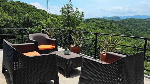 An outdoor seating area with wicker furniture and potted plants, overlooking a lush green landscape and a distant tower.