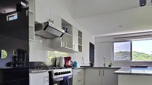 A modern kitchen with white cabinets, a stove, and a window overlooking a green landscape.