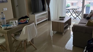 A modern living room with a flat-screen TV, a dining table with chairs, a sofa, and a balcony with a table and chairs. - Hotel Onyx (Belgrade)