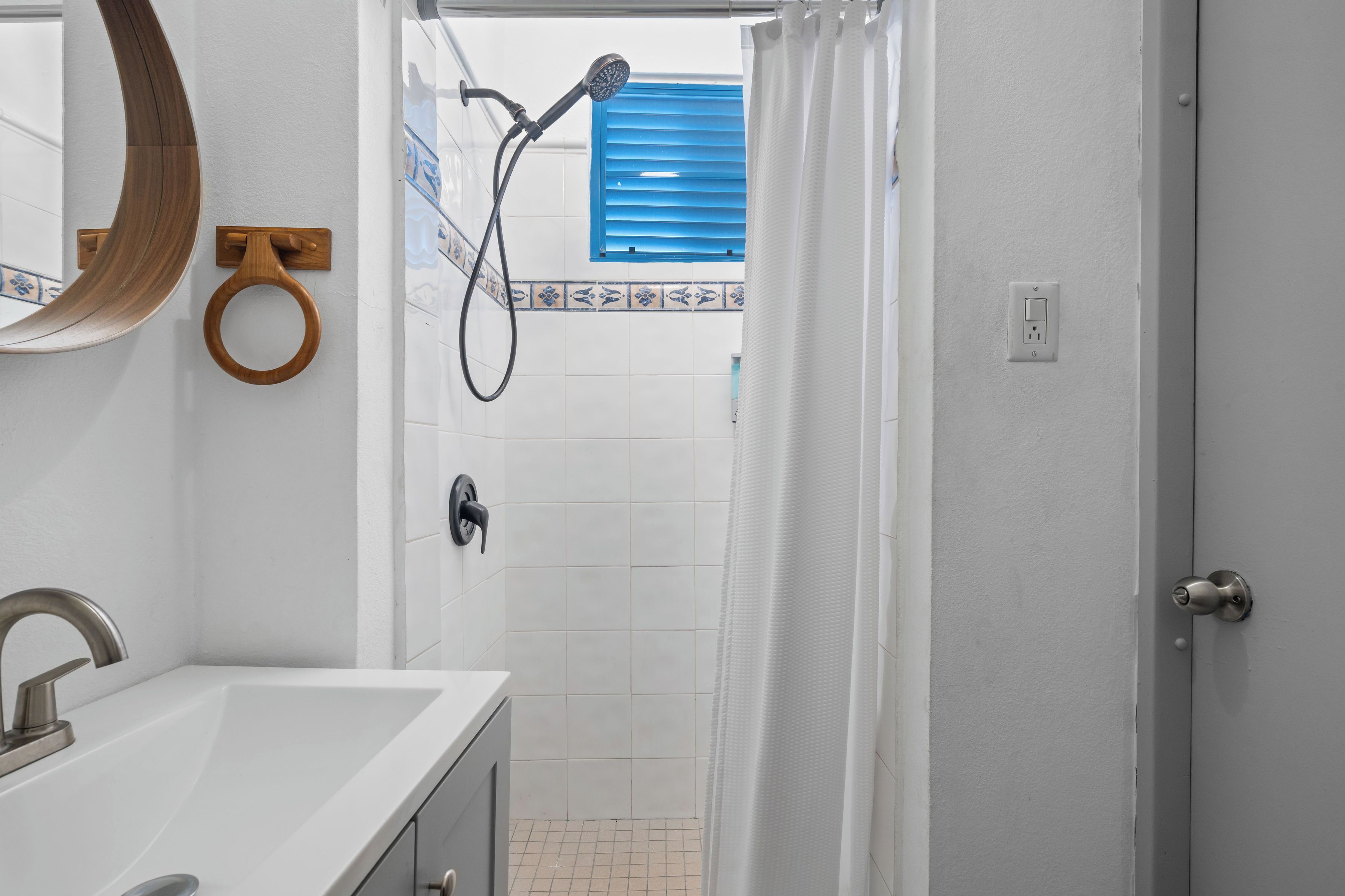 A bathroom with a sink, mirror, shower, and a door leading to another room.