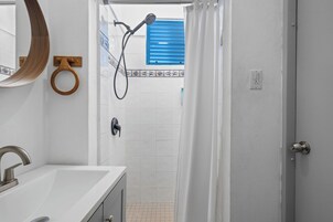 Un baño con lavamanos, espejo, ducha y puerta que da a otra habitación.