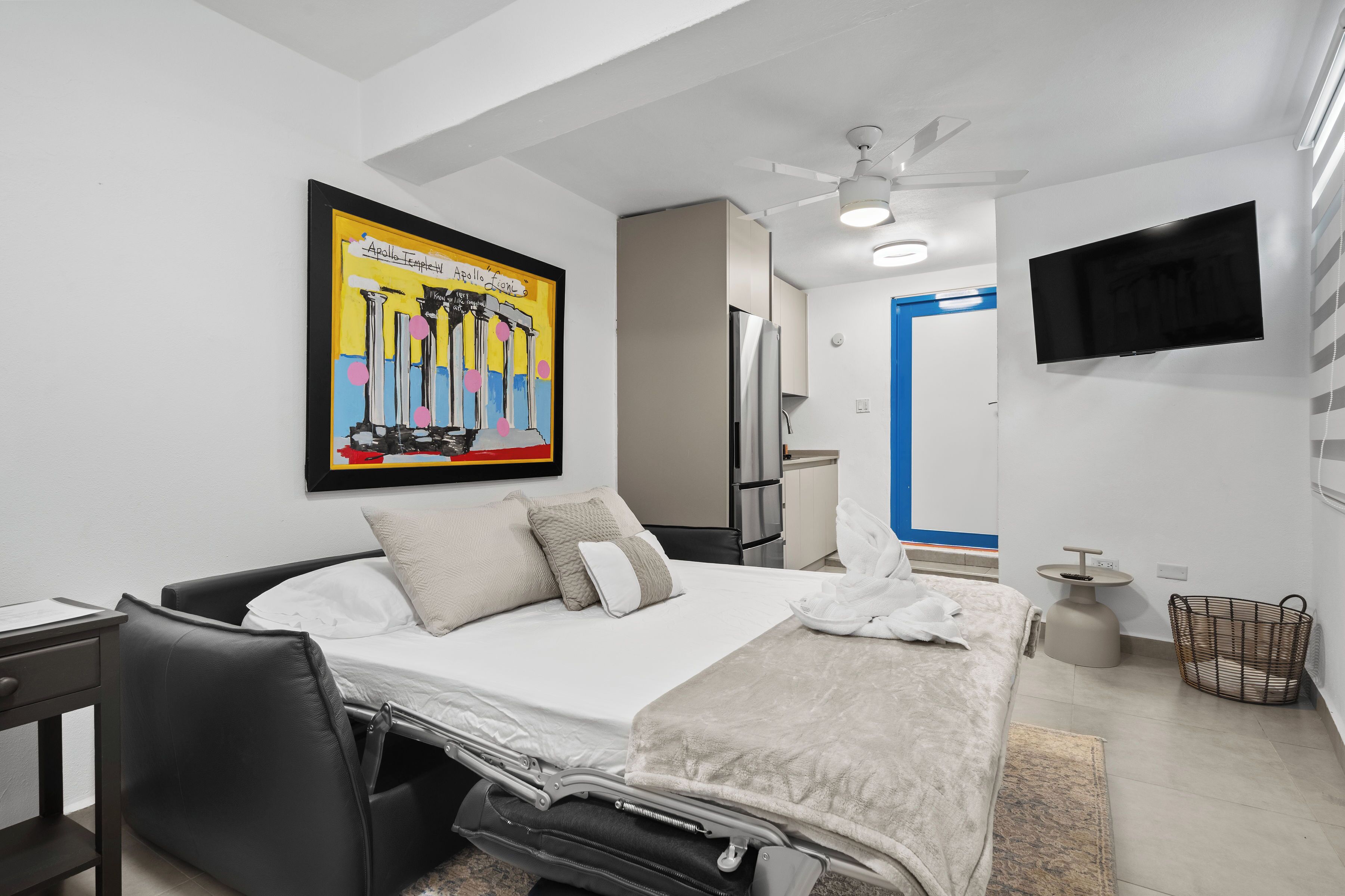 Une chambre d’hôtel moderne équipée d’un lit, d’un bureau, d’une chaise, d’un téléviseur fixé au mur et d’un ventilateur de plafond.