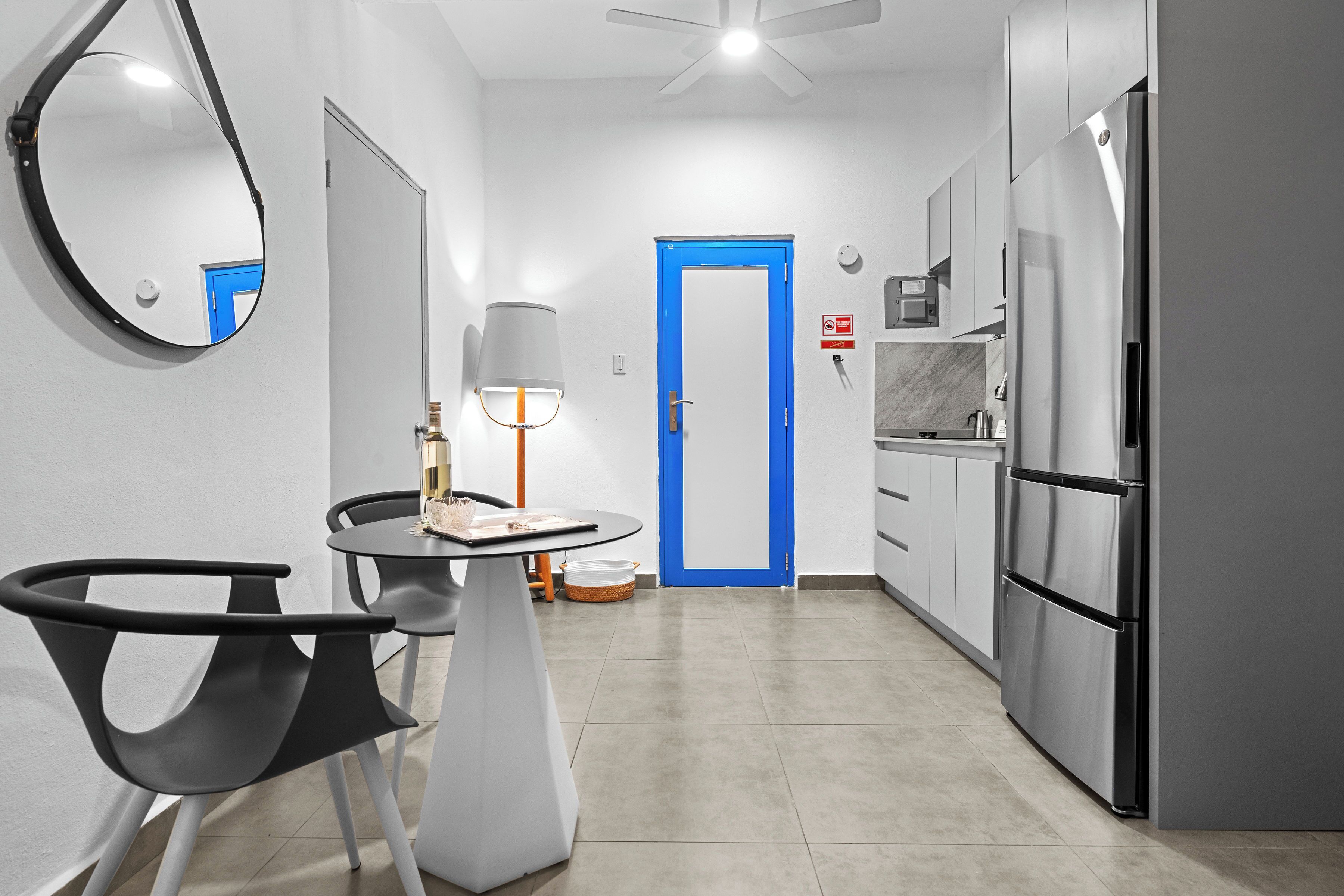 A modern kitchen with a blue door, a refrigerator, and a dining area with a table and chairs.