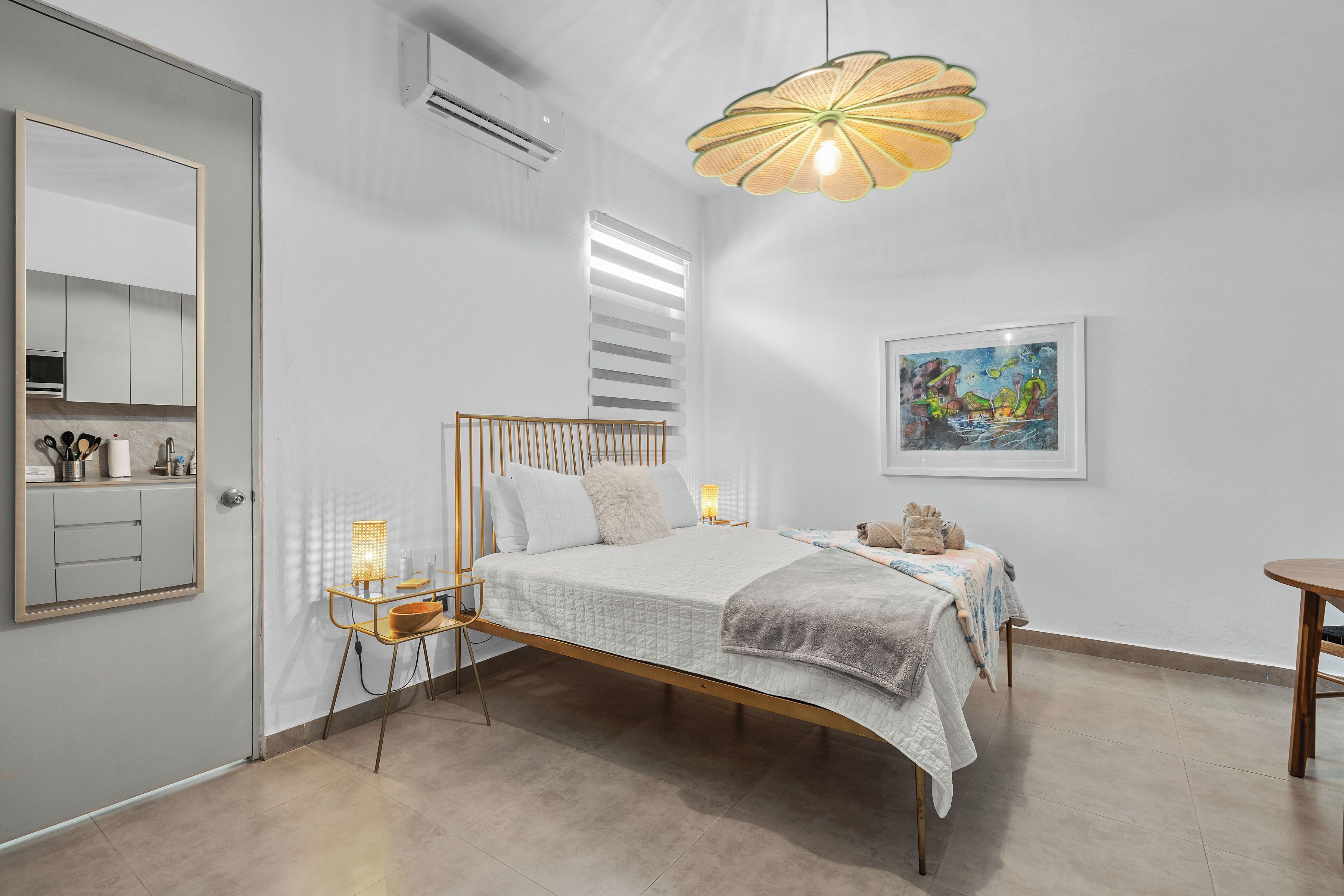 Un dormitorio con cama, mesitas de noche, un espejo, aire acondicionado, una lámpara colgante y un cuadro en la pared.