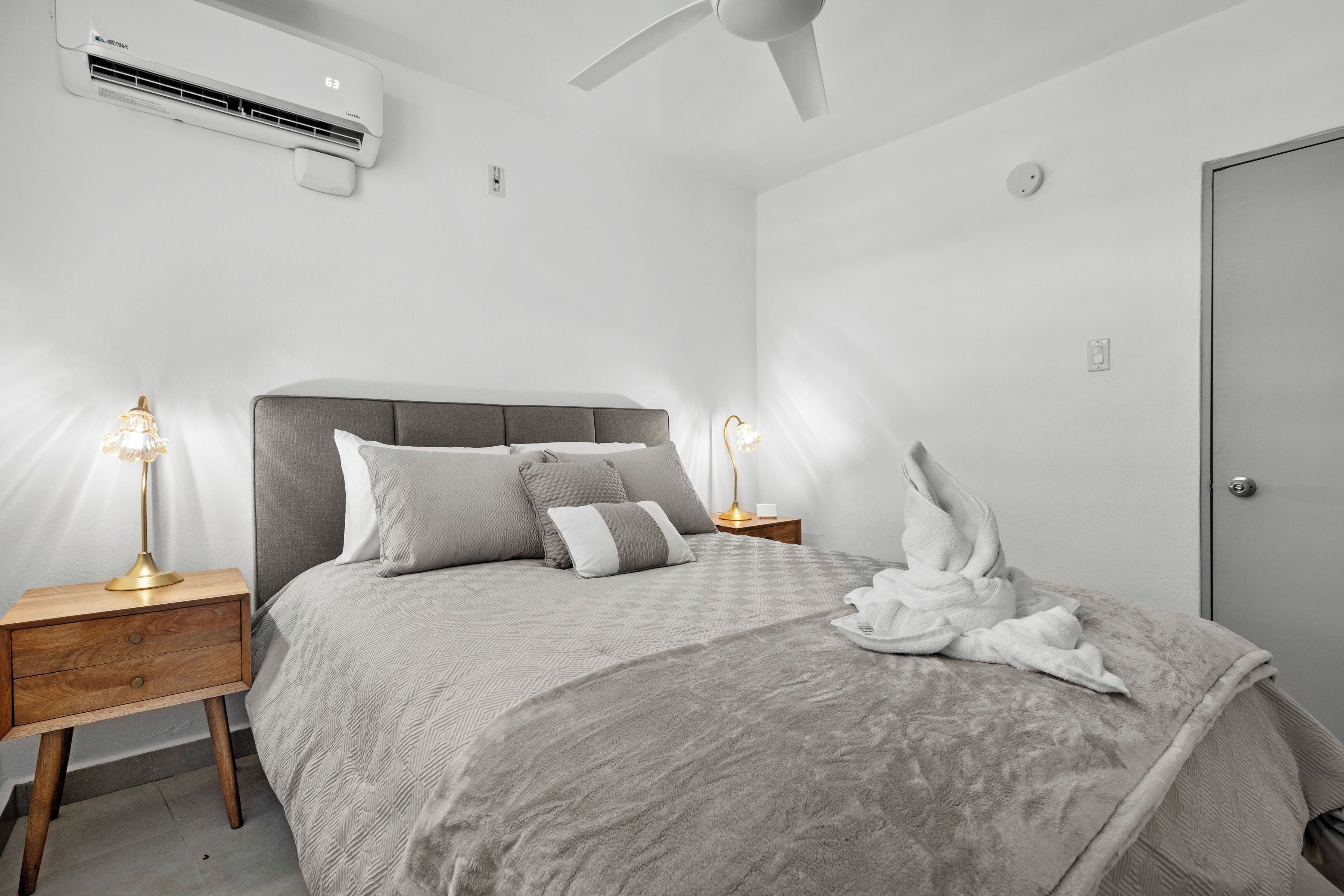 Ein modernes Schlafzimmer mit Bett, Nachttischen, Deckenventilator und Klimaanlage.