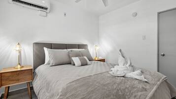 Ein modernes Schlafzimmer mit Bett, Nachttischen, Deckenventilator und Klimaanlage.