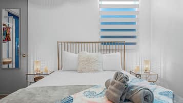 A hotel room with a bed, a window with blinds, a bedside table with a lamp, and a towel on the bed.